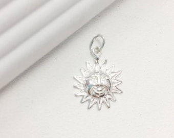 May include: A silver charm in the shape of a sun with a face. The sun has a smiling face with a small nose and eyes.
