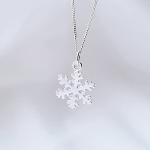May include: A silver snowflake pendant necklace on a white background. The snowflake is a delicate design with intricate details.