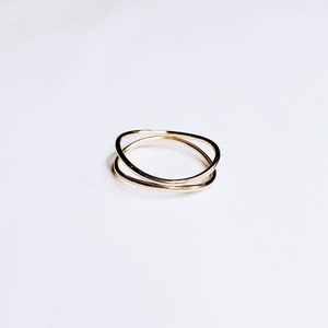 May include: A gold-toned ring with two bands that are intertwined. The bands are smooth and have a slightly irregular shape.