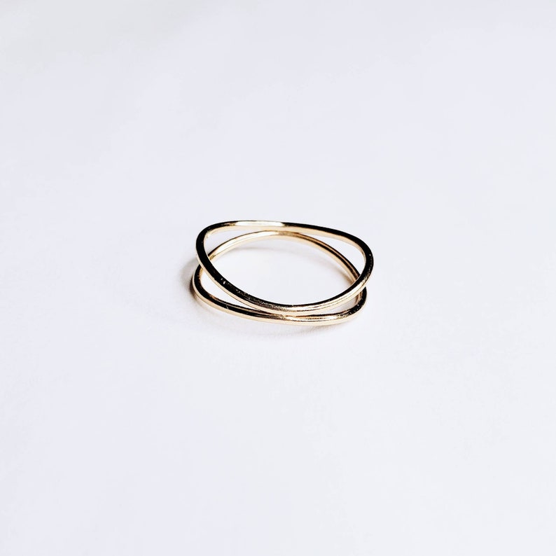 May include: A gold-toned ring with two bands that are intertwined. The bands are smooth and have a slightly irregular shape.