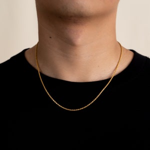 May include: A gold rope chain necklace worn by a person wearing a black shirt.