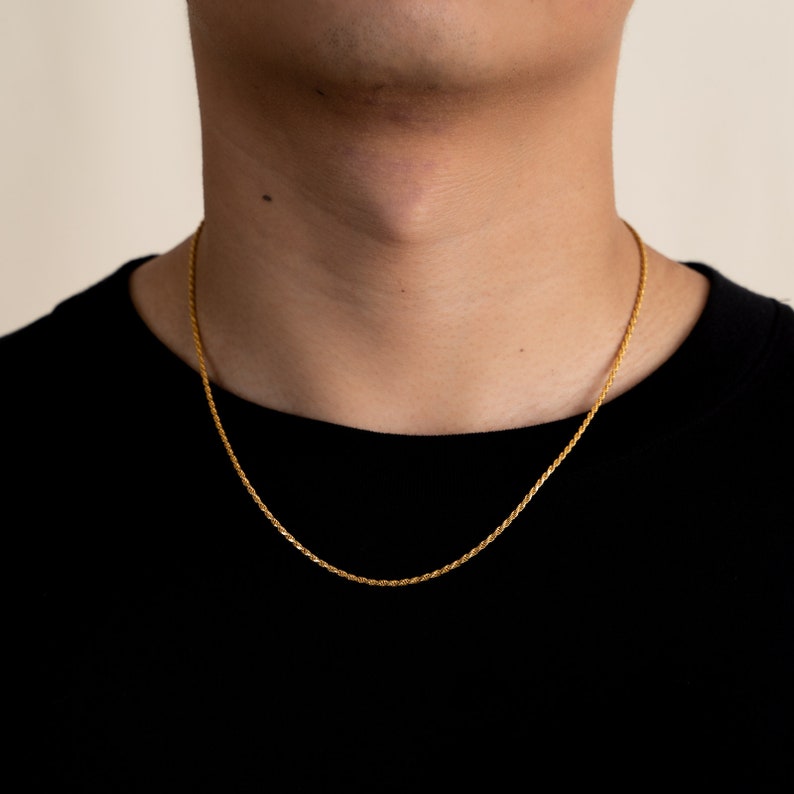May include: A gold rope chain necklace worn by a person wearing a black shirt.