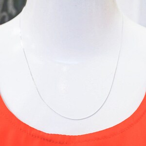 May include: A silver chain necklace on a white mannequin wearing a red shirt.