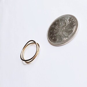 May include: Two thin gold rings, one slightly larger than the other, are intertwined. The rings are shown next to a Canadian 25-cent coin.