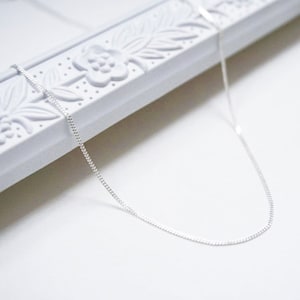 May include: A silver chain necklace on a white background.
