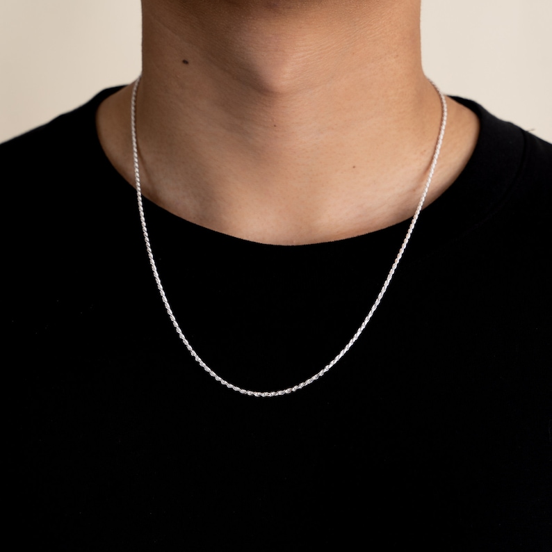 May include: A silver rope chain necklace worn by a person wearing a black shirt.