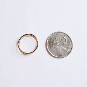 May include: A thin gold ring, shown next to a Canadian 25 cent coin, to show the size of the ring.