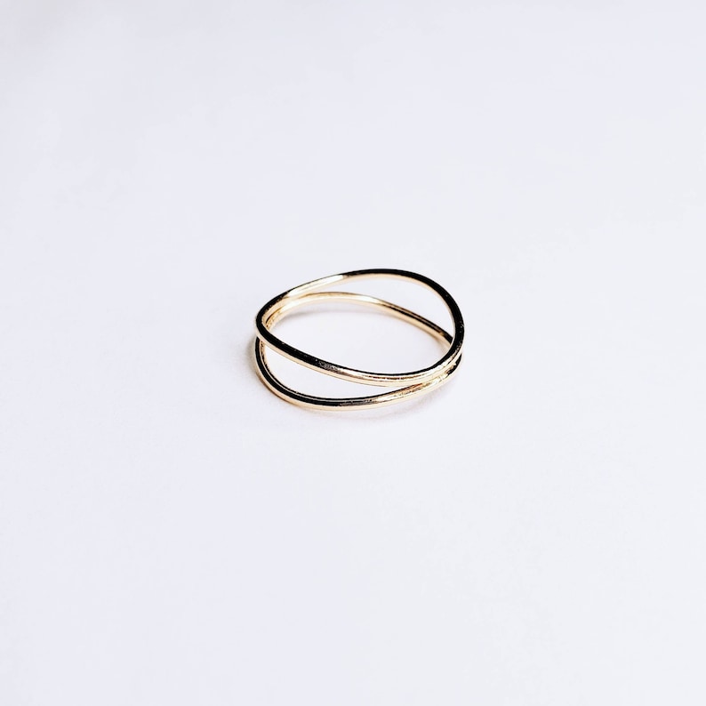 May include: A gold-toned ring with a simple, minimalist design. The ring features two bands that cross over each other, creating a delicate and modern look.