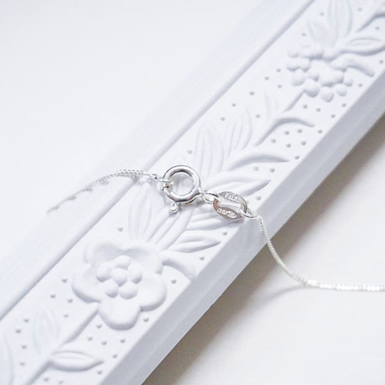 May include: A silver chain necklace with a lobster clasp closure. The clasp has the words "925 Italy" engraved on it.