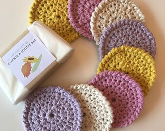 May include: A set of eight crocheted makeup remover pads in shades of yellow, pink, and purple. The pads are arranged in a circle around a small bar of soap with a label that reads "The Soap Loaf Co. Cleanse & Soothe Bar".