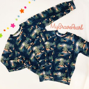 Op de afbeelding: Twee marineblauwe longsleeves met een winterbosprint met bomen, herten, vossen en een volle maan. De print is in tinten groen, bruin en wit. De tekst "MyBravePearl" is zichtbaar op het bovenste sweatshirt.