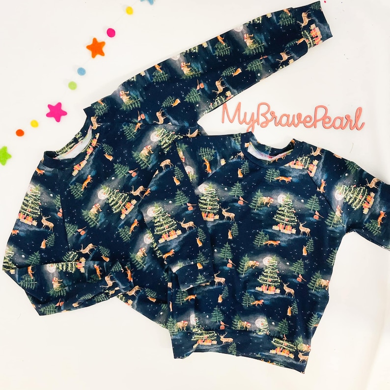Op de afbeelding: Twee marineblauwe longsleeves met een winterbosprint met bomen, herten, vossen en een volle maan. De print is in tinten groen, bruin en wit. De tekst "MyBravePearl" is zichtbaar op het bovenste sweatshirt.