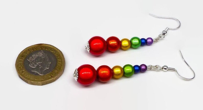 May include: Rainbow colored beaded dangle earrings with silver hooks. The beads are red, orange, yellow, green, blue, and purple. The earrings are about the size of a US one pound coin.