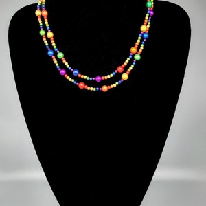May include: A multi-strand necklace with rainbow colored beads. The necklace is made of small, round beads in shades of red, orange, yellow, green, blue, indigo, and violet.