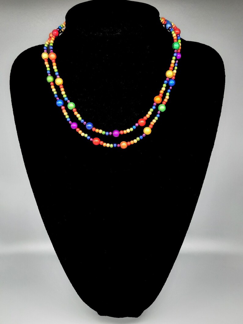 May include: A multi-strand necklace with rainbow colored beads. The necklace is made of small, round beads in shades of red, orange, yellow, green, blue, indigo, and violet.