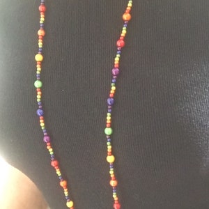 May include: A long necklace made of colorful beads. The beads are arranged in a rainbow pattern, with purple, blue, green, yellow, orange, and red beads.