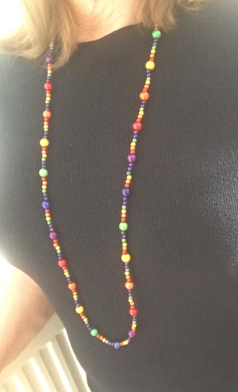 May include: A long necklace made of colorful beads. The beads are arranged in a rainbow pattern, with purple, blue, green, yellow, orange, and red beads.