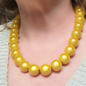 Peut inclure: Un collier en or composé de grosses perles rondes. Les perles sont brillantes et ont un léger reflet métallique.