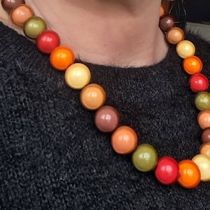 May include: A necklace made of round, colorful wooden beads. The beads are in shades of brown, orange, red, and green. The necklace is worn by a person, but the person's face is not visible.
