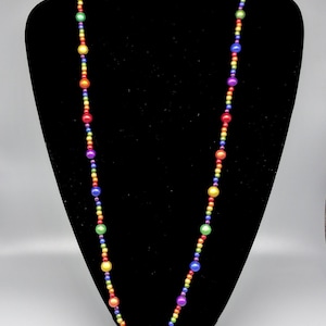 May include: A long rainbow beaded necklace with round, iridescent beads. The necklace is displayed on a black velvet bust form.