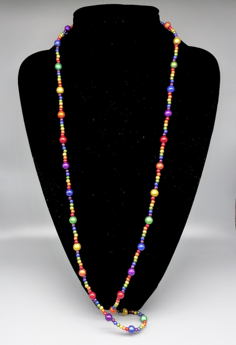 May include: A long rainbow beaded necklace with round, iridescent beads. The necklace is displayed on a black velvet bust form.
