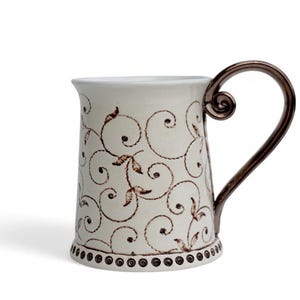 May include: A white ceramic mug with a brown floral design and a copper-colored handle. The mug has a beaded rim.