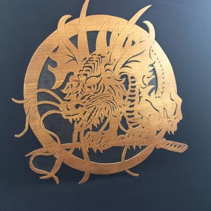 May include: A wooden wall art piece featuring a detailed carving of a dragon's head with a sword in its mouth. The dragon is surrounded by a circular frame.