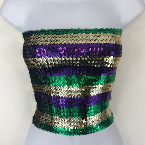 May include: A strapless sequin top in a vibrant color scheme of green, gold, and purple. The top is made of small, round sequins arranged in horizontal stripes. The garment is displayed on a white mannequin, showcasing its form and design.