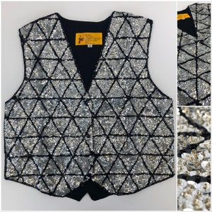 May include: A silver sequined vest with a geometric triangle pattern outlined in black. The vest has a V-neck and a black back. A small yellow tag with text is visible near the neckline. The vest is a size small.