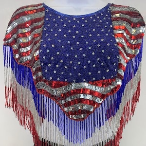 May include: A beaded shawl with a fringe border in red, white, and blue, featuring a sequined American flag design.