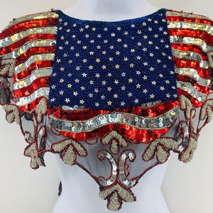 May include: A red, white, and blue sequined American flag design on a black mesh fabric. The design is a traditional American flag with stars and stripes.