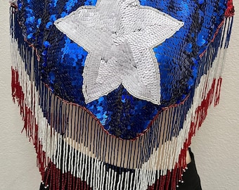 May include: A sequined top with a large white star on a blue background, red and white stripes, and beaded fringe. The top is a patriotic design, likely for a special occasion or themed event.