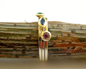 May include: Three gold rings with different colored gemstones. The top ring has a green gemstone, the middle ring has a blue gemstone, and the bottom ring has a pink gemstone.