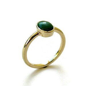 Puede incluir: Un anillo de oro con una piedra preciosa ovalada verde. El anillo es simple y elegante.