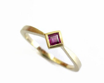 May include: A gold ring with a small, square, pink gemstone set in the center.