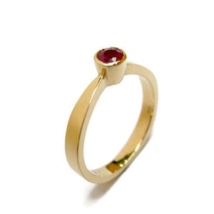 May include: A simple gold band ring with a single red gemstone.