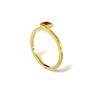May include: A gold ring with a small, square, red gemstone set in the center.