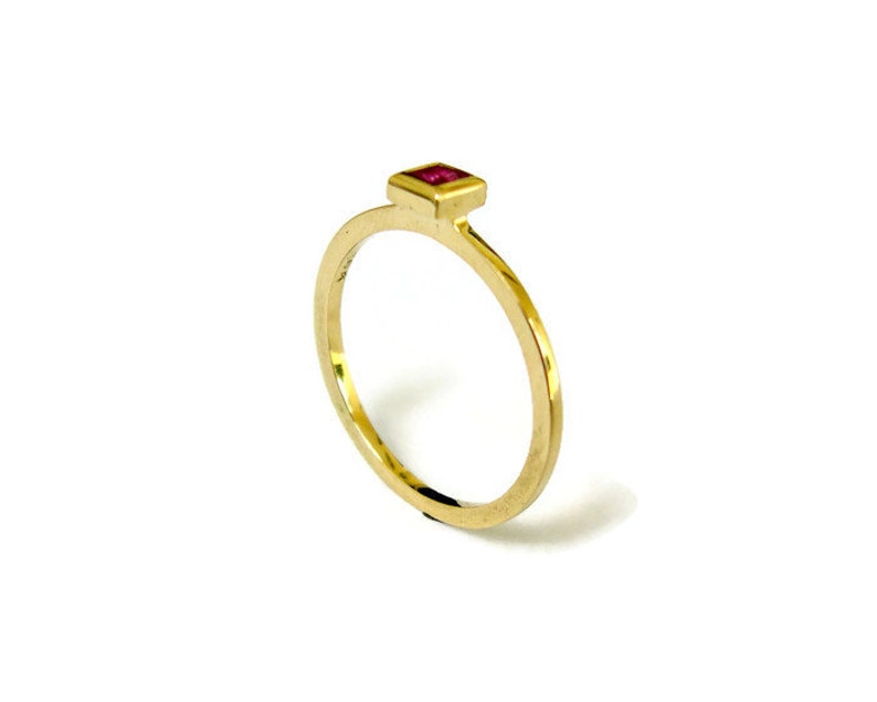 May include: A gold ring with a small, square, red gemstone set in the center.