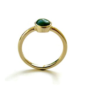 Puede incluir: Un anillo de oro con una piedra preciosa ovalada verde engastada en el centro.