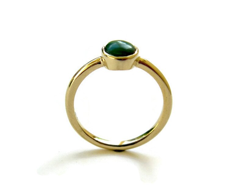 Puede incluir: Un anillo de oro con una piedra preciosa ovalada verde engastada en el centro.