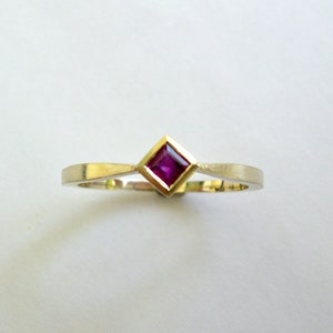 May include: A simple gold band ring with a small square-shaped ruby gemstone set in the center.