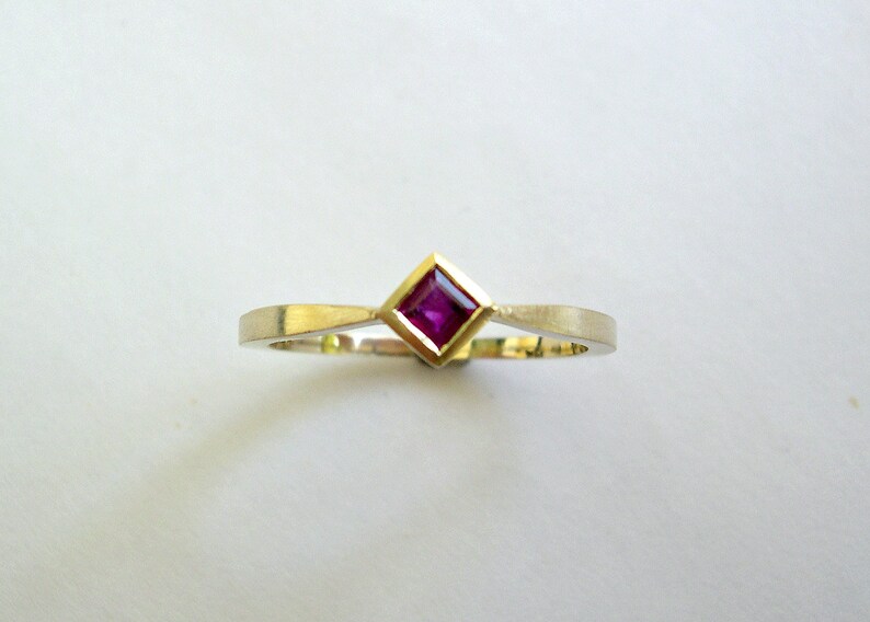 May include: A simple gold band ring with a small square-shaped ruby gemstone set in the center.