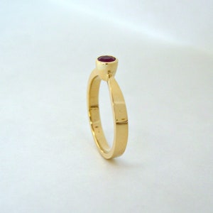 May include: A simple gold band ring with a single red gemstone set in the center.