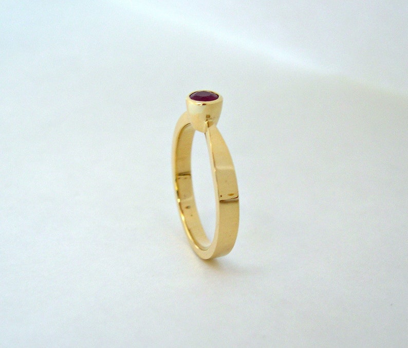 May include: A simple gold band ring with a single red gemstone set in the center.