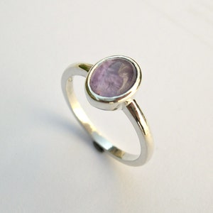 May include: A silver ring with a light purple oval gemstone.