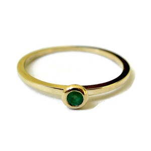 May include: A simple gold band ring with a single round emerald green gemstone.