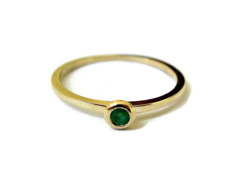 May include: A simple gold band ring with a single round emerald green gemstone.