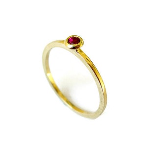 May include: A simple gold band ring with a single red gemstone set in the centre.