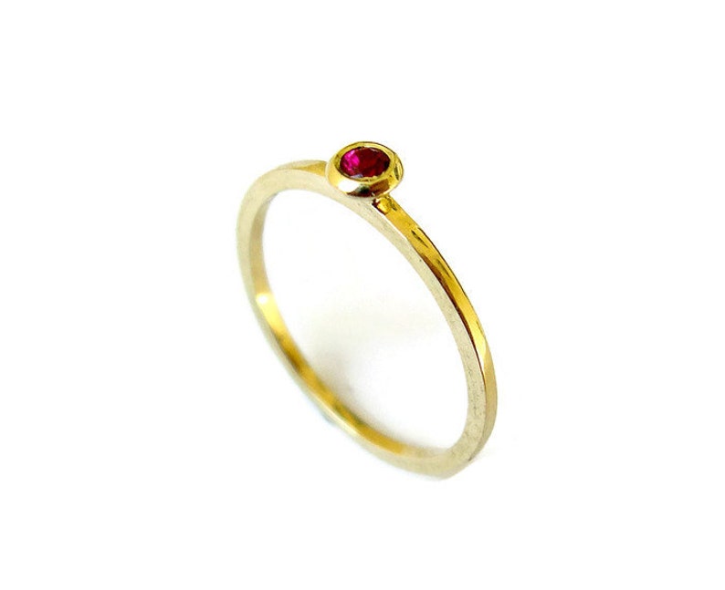 May include: A simple gold band ring with a single red gemstone set in the centre.