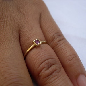 May include: A gold ring with a small square-shaped pink gemstone.